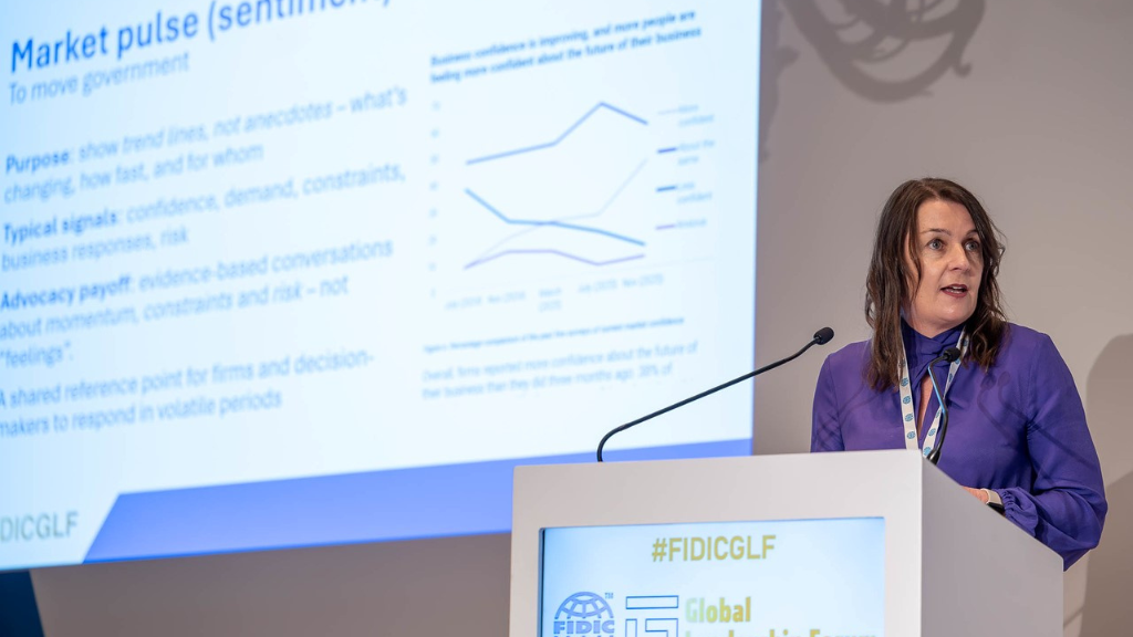 Helen Davidson speaks at the FIDC conference in front of a screen in a purple dress.