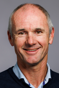 White male, smiling, headshot, light blue collared shirt.
