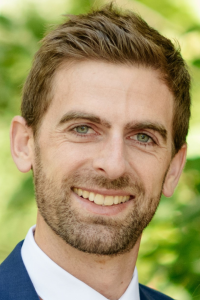 White male, headshot, beard, smiling, suit.
