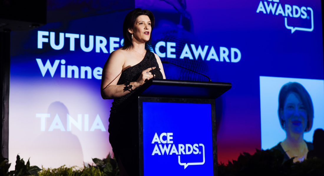 White female, shoulder length brown hair, evening dress, standing at podium receiving award.