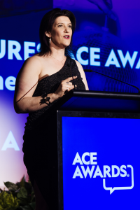 White female, short dark hair, evening dress, awards ceremony, standing at podium.