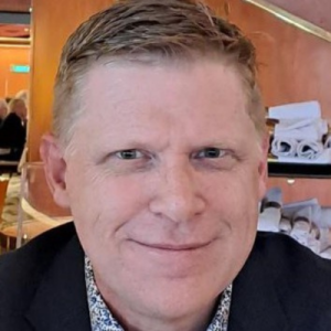White male, fair hair, smiling, suit, headshot.