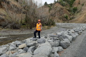 White female, high vis, standing at river bed.