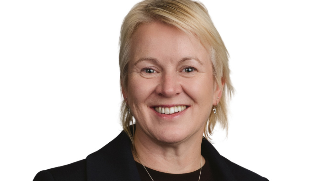 White female, short blonde hair, earrings, smiling, suit.