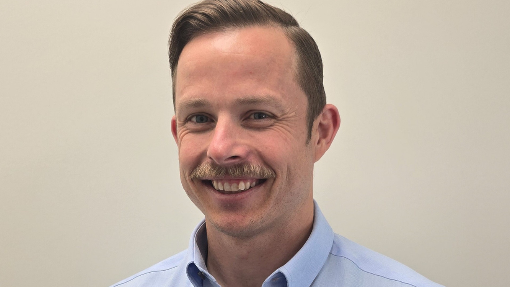 White male, fair hair, moustache, smiling, blue shirt.