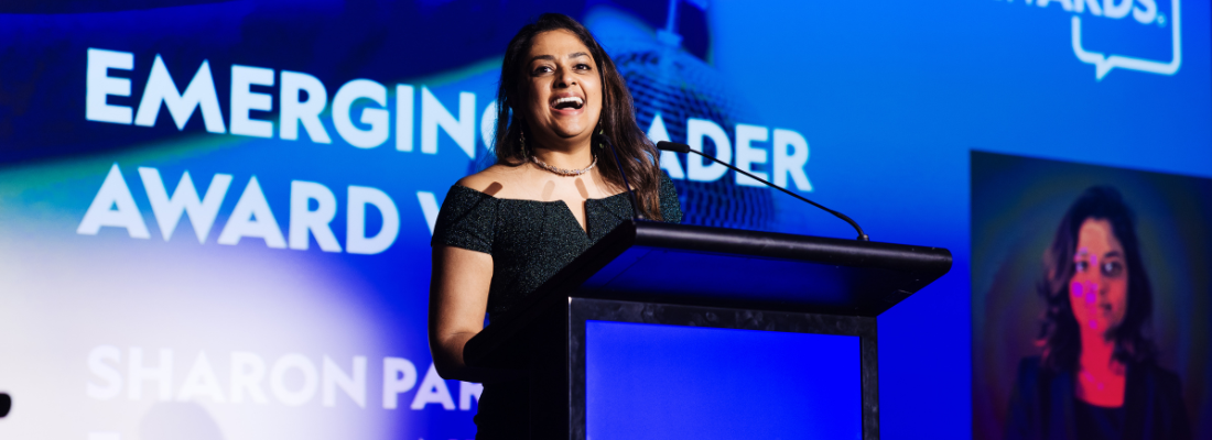 Dark skinned female, shoulder length dark hair, smiling, evening dress, standing at awards podium.