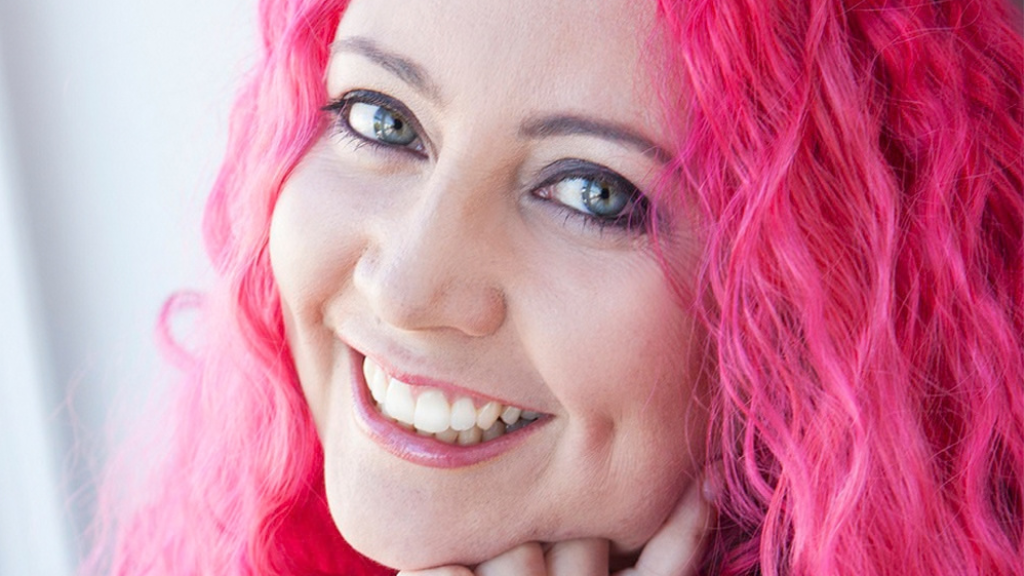 White female, pink wavy hair, green eyes, smiling.