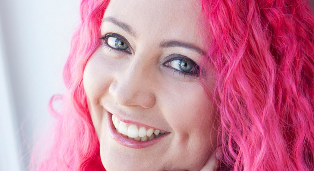White female, pink wavy hair, green eyes, smiling.