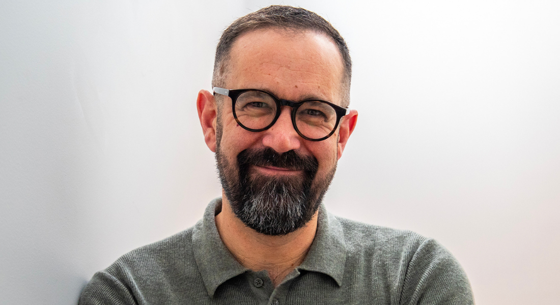 White male, dark hair and beard, glasses, smiling, grey polo shirt, headshot.