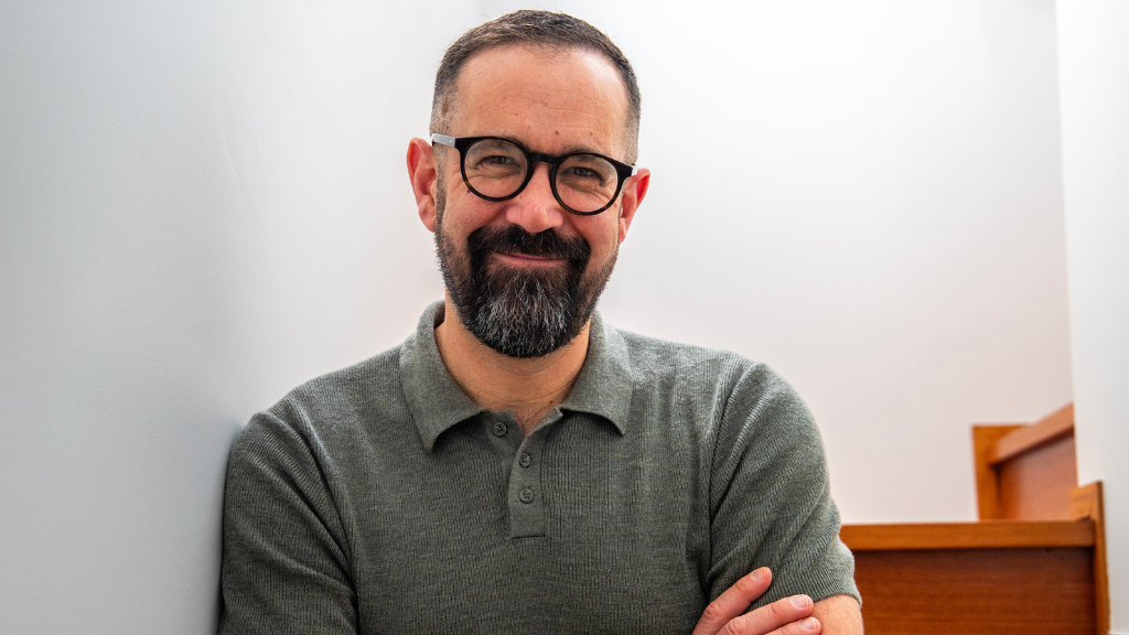 White male, dark beard, smiling, glasses, grey polo shirt.